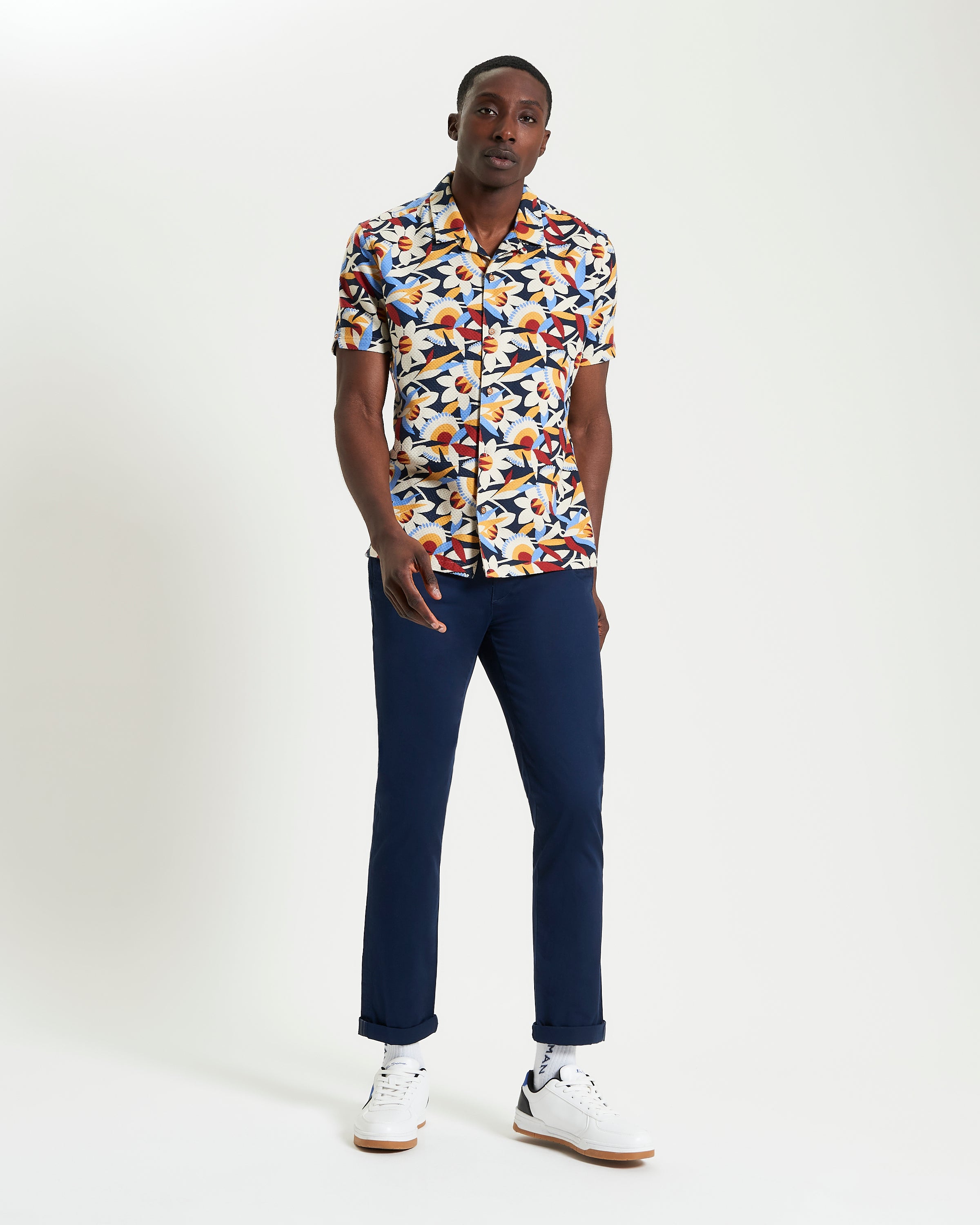 Abstract Floral Print – Bold pattern short-sleeve shirt model wearing navy trousers and white sneakers.