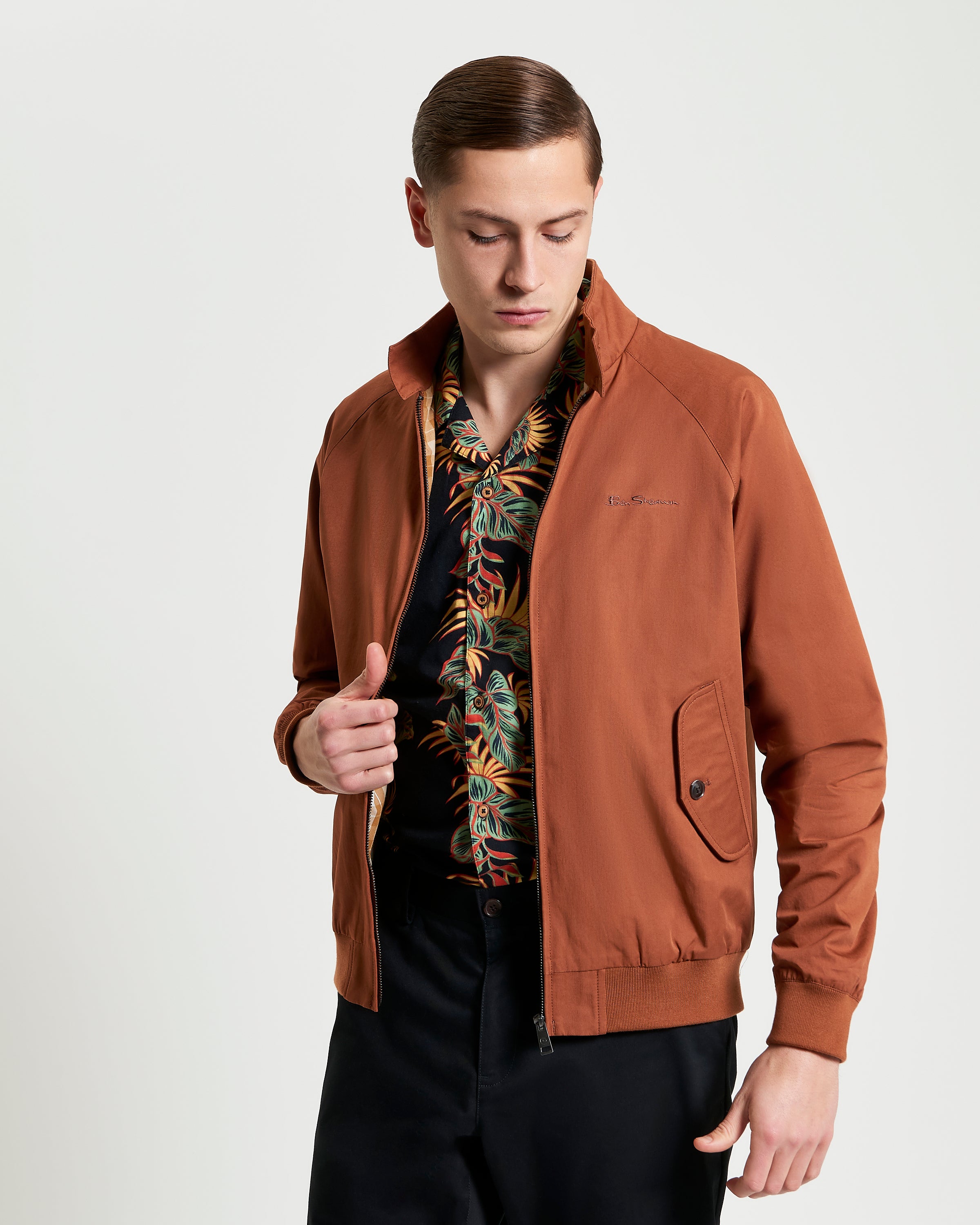 Model wearing a brown Signature Harrington Jacket over a vibrant floral shirt, showcasing classic British style.