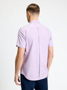 Back view of a man wearing the Signature Oxford Short Sleeve Shirt in light purple, featuring a button-down collar and back pleat.