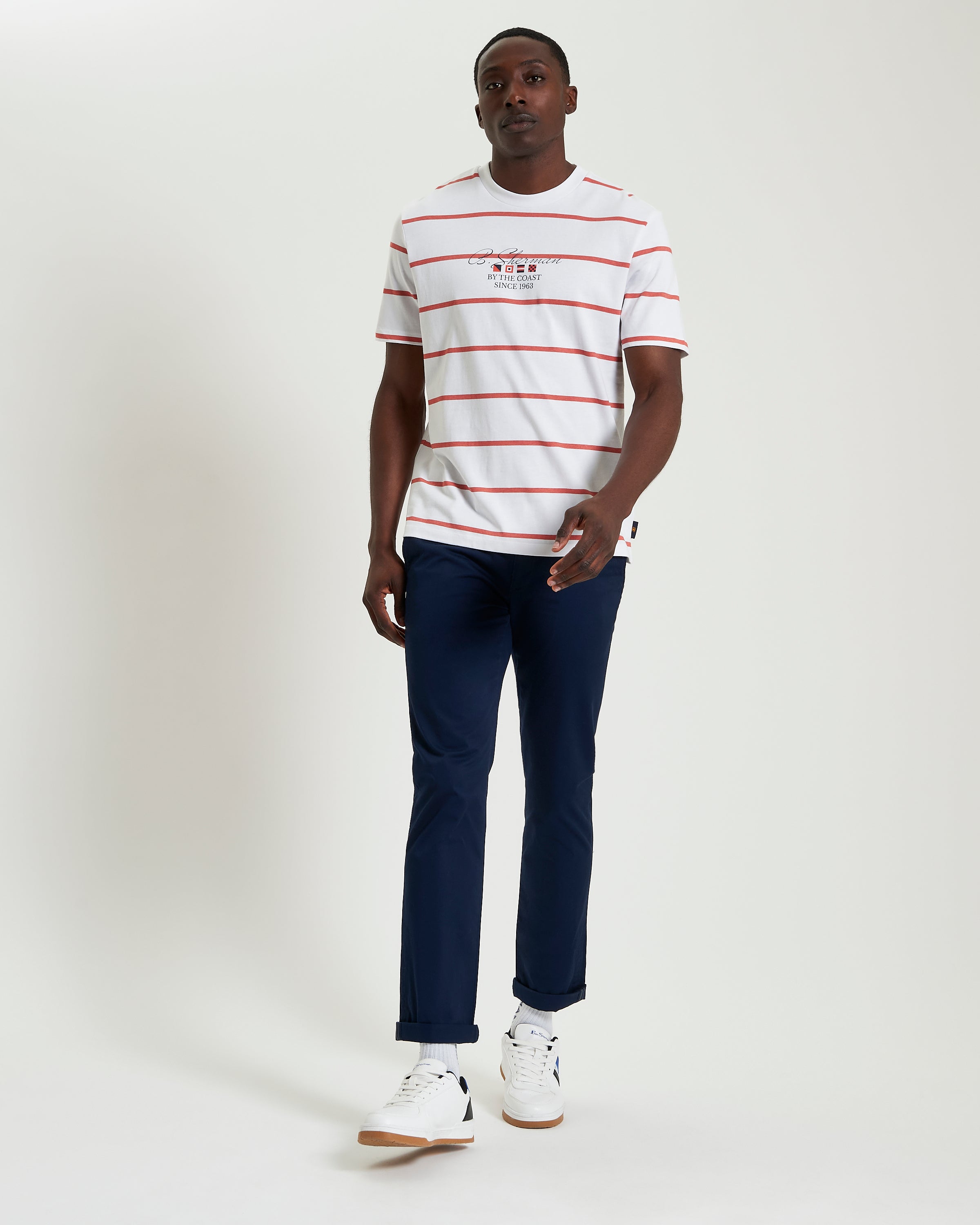 Model wearing Stripe Script shirt with red and white stripes, paired with navy trousers and sneakers.