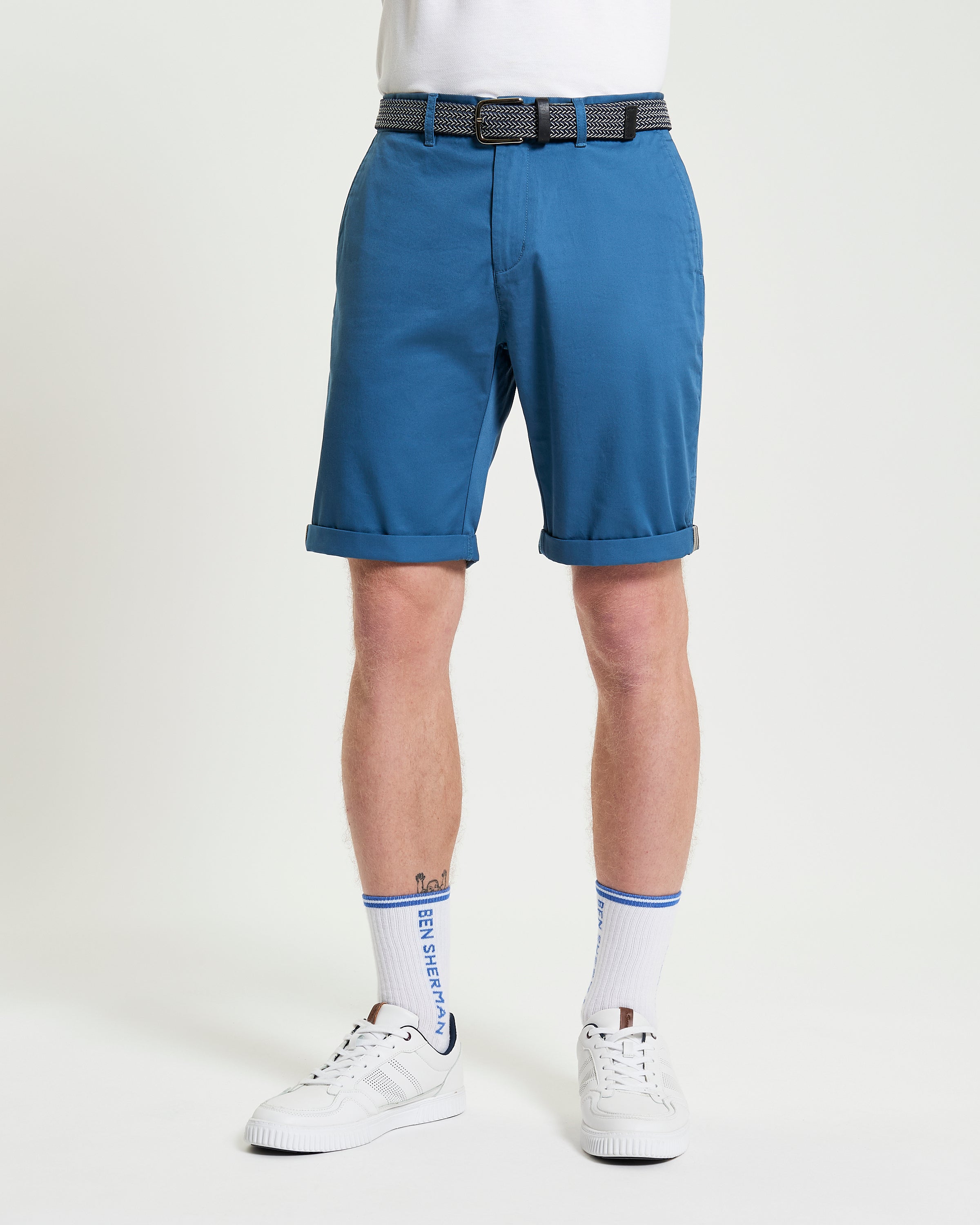 Signature Chino Short – blue chino shorts with rolled hem, paired with a belt and white sneakers.