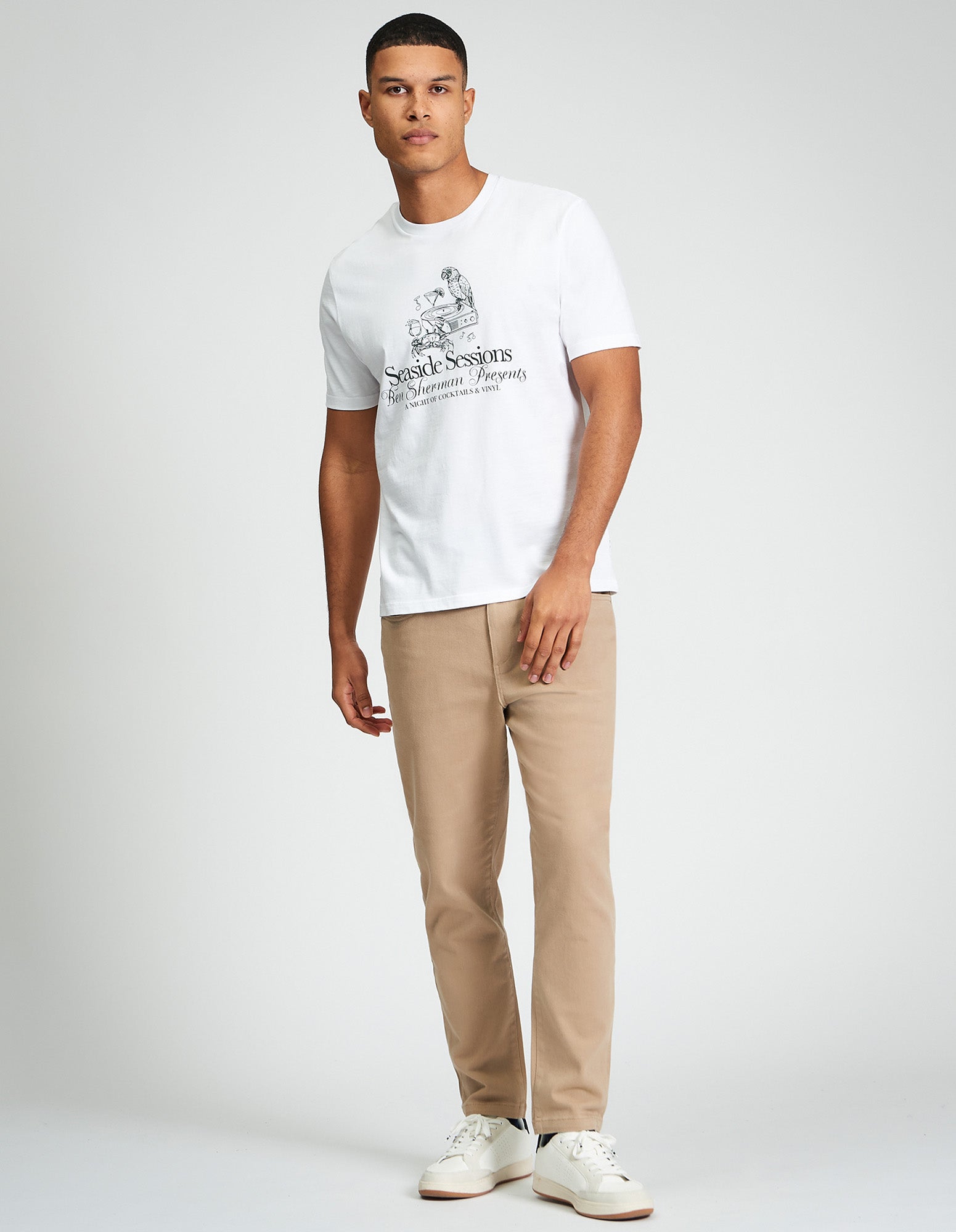 Man wearing Seaside Sessions Tee, a white organic cotton t-shirt with graphic print, styled with beige trousers.